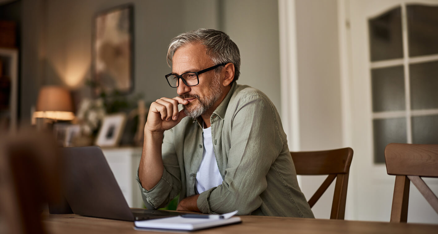 A man at a desk observing his laptop in deep thought